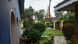 A courtyard with a stone pathway, lush greenery, and a distant temple structure. - Baia Do Sol - Beach Boutique (Baga)