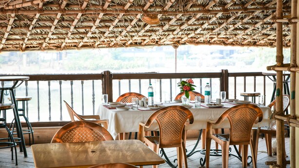 An outdoor dining area with bamboo ceiling and wooden furniture, overlooking a body of water. - Baia Do Sol - Beach Boutique (Baga)