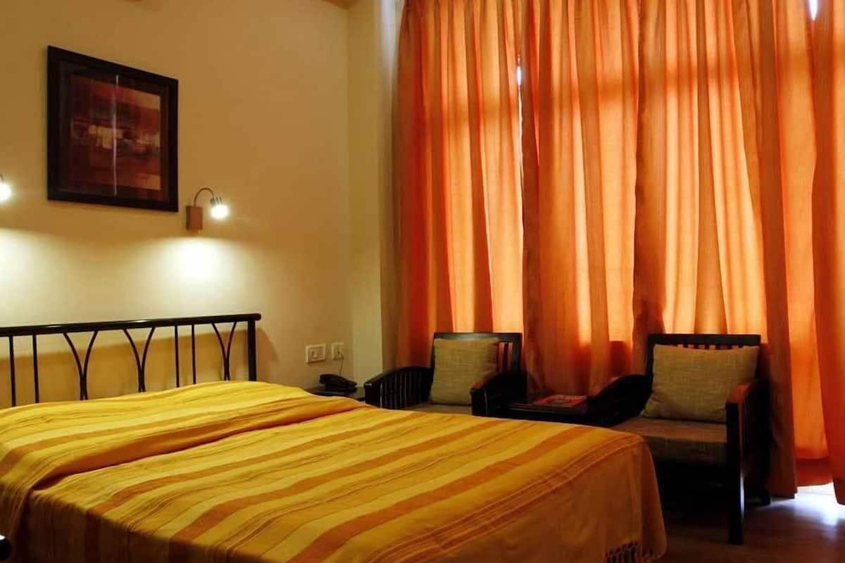 A hotel room with two beds, a chair, and orange curtains.