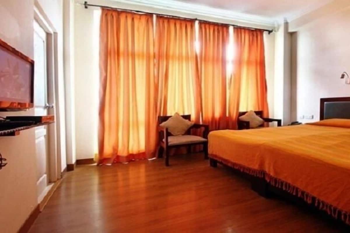 A hotel room with a large bed, two chairs, a desk, and a window with orange curtains.