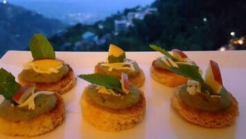 Una mesa con cinco aperitivos dispuestos en un plato blanco, con un paisaje montañoso de fondo.