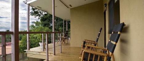 A wooden deck with two chairs and a table, overlooking a garden and a building.