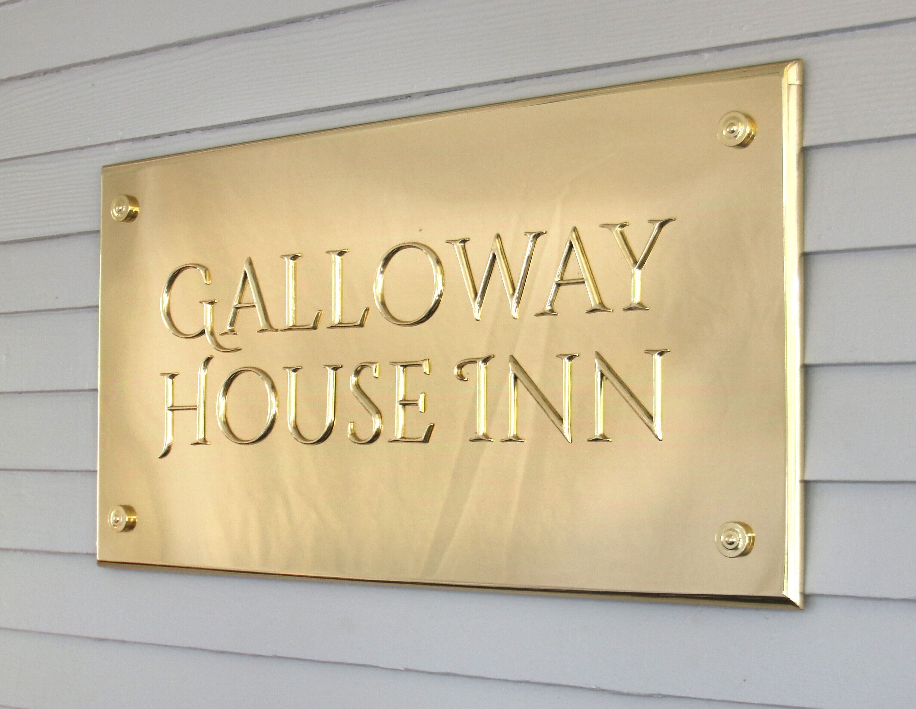 Une plaque en laiton portant l’inscription « Galloway House Inn » est fixée à un mur de couleur claire.
