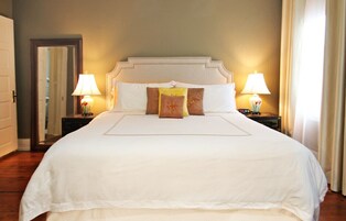 A large bed with a white headboard, two bedside lamps, and a mirror on the wall.