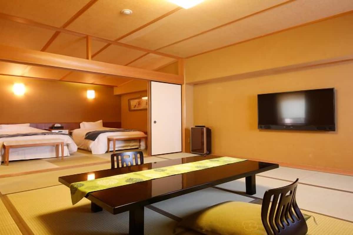 Habitación de hotel con dos camas, un televisor de pantalla plana, una mesa de madera y esteras de tatami.