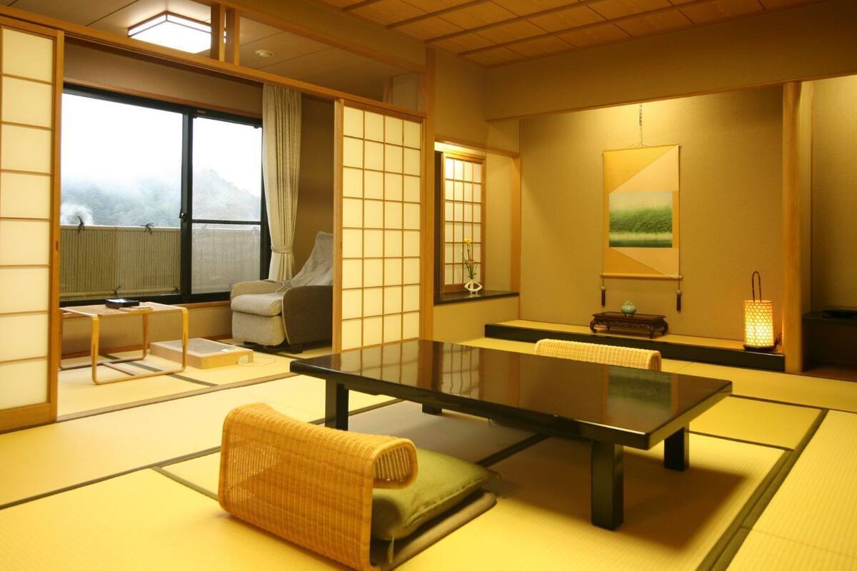 Habitación con esteras de tatami, una mesa baja, un cojín, una silla y vistas al exterior.