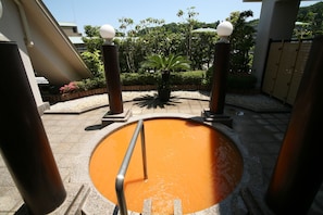 A circular pool with a metal railing, surrounded by a paved area with a palm tree and a fence.