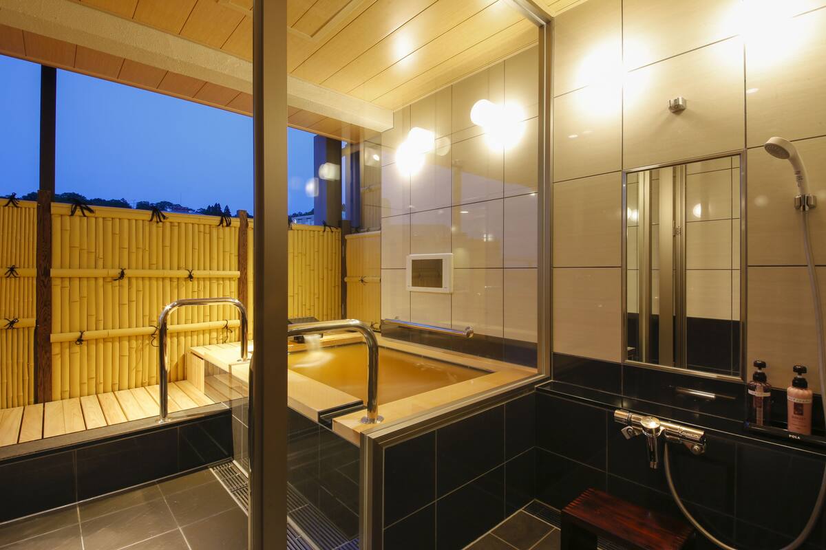 Un baño moderno con una zona de baño de madera, ducha con cerramiento de vidrio y espejo con artículos de aseo.