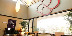 A hotel lobby with a reception desk, seating area, large windows, and a decorative wall with a logo.