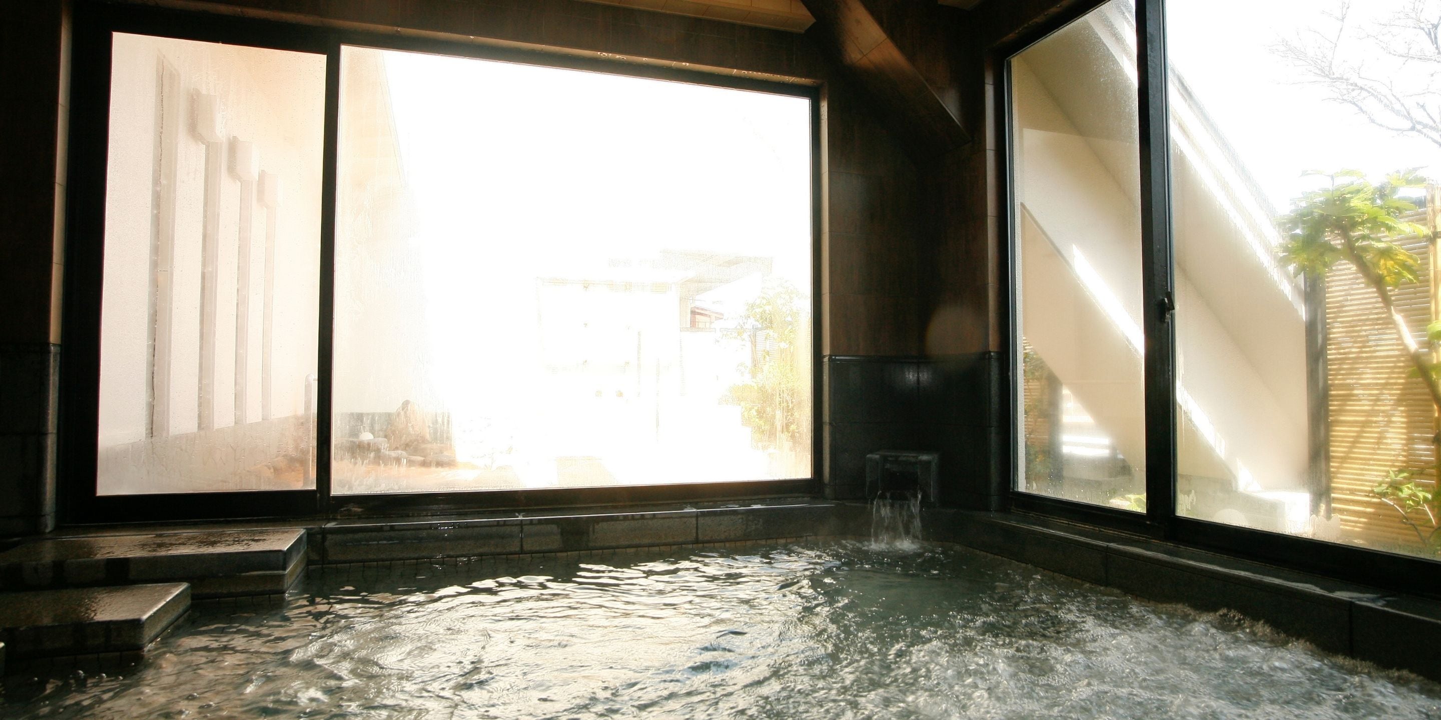 A hot spring bath with a view of a traditional building through large windows.