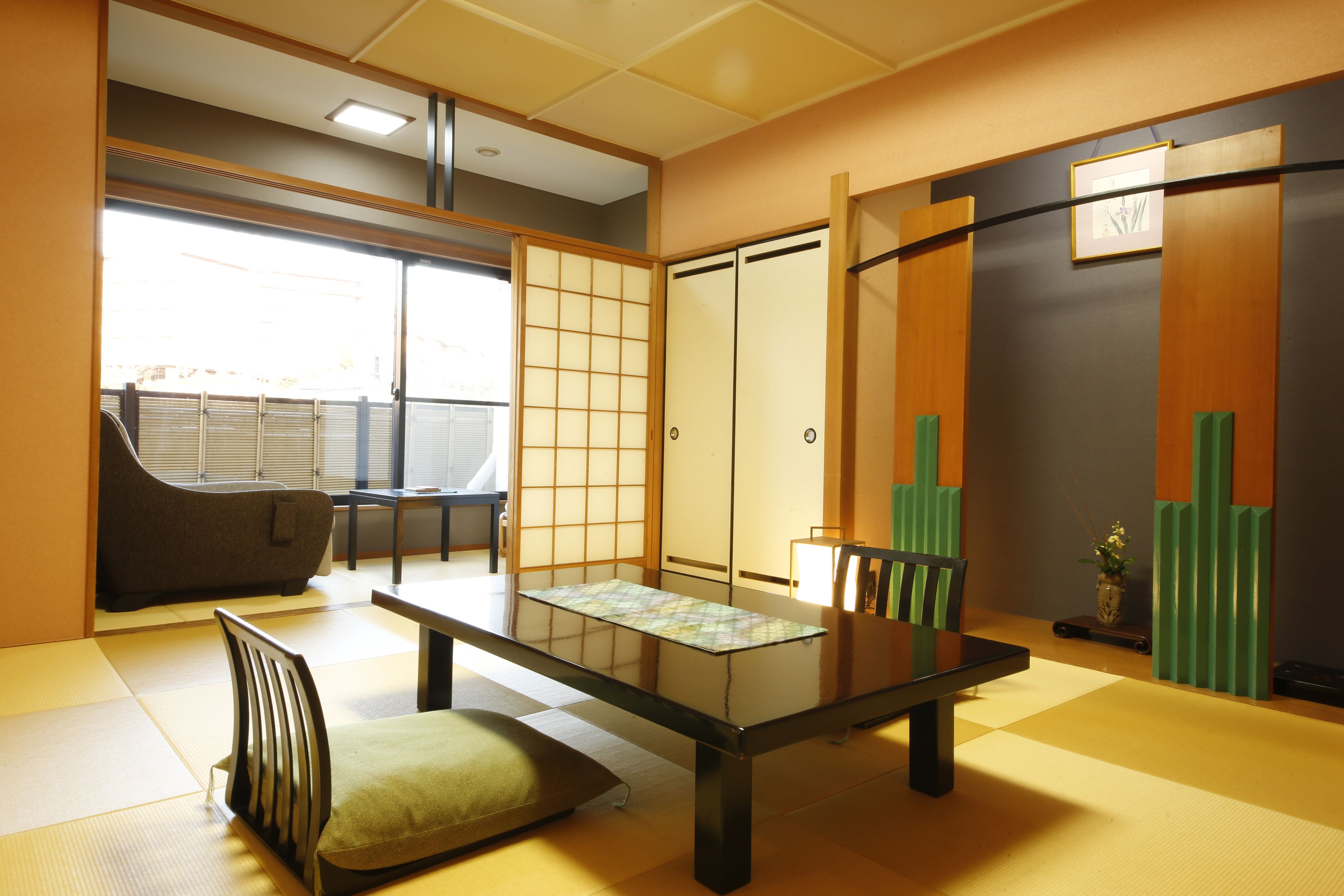Ein traditioneller japanischer Raum mit Tatami-Boden, einem niedrigen Tisch, einem gepolsterten Sessel, Schiebetüren und Blick durch ein Fenster.