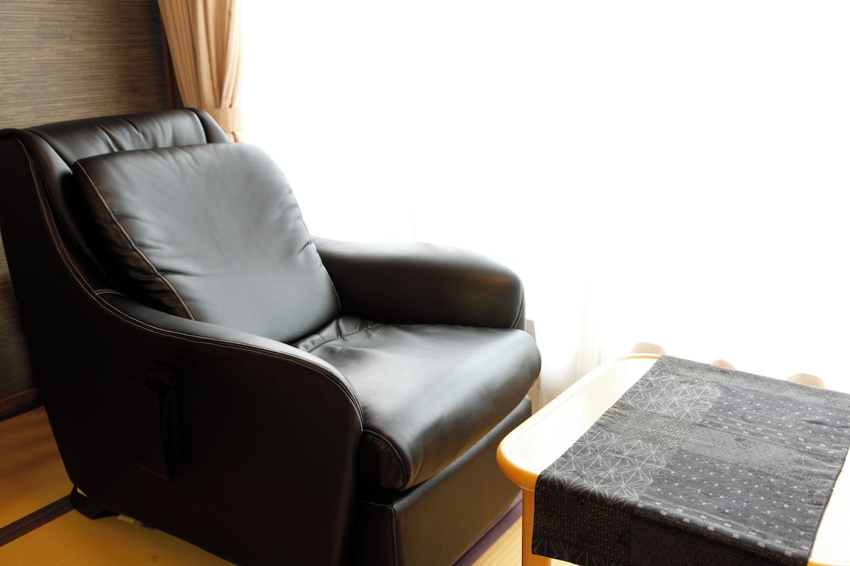 Un sofá de cuero negro en una habitación con suelo de madera y una ventana con cortinas.