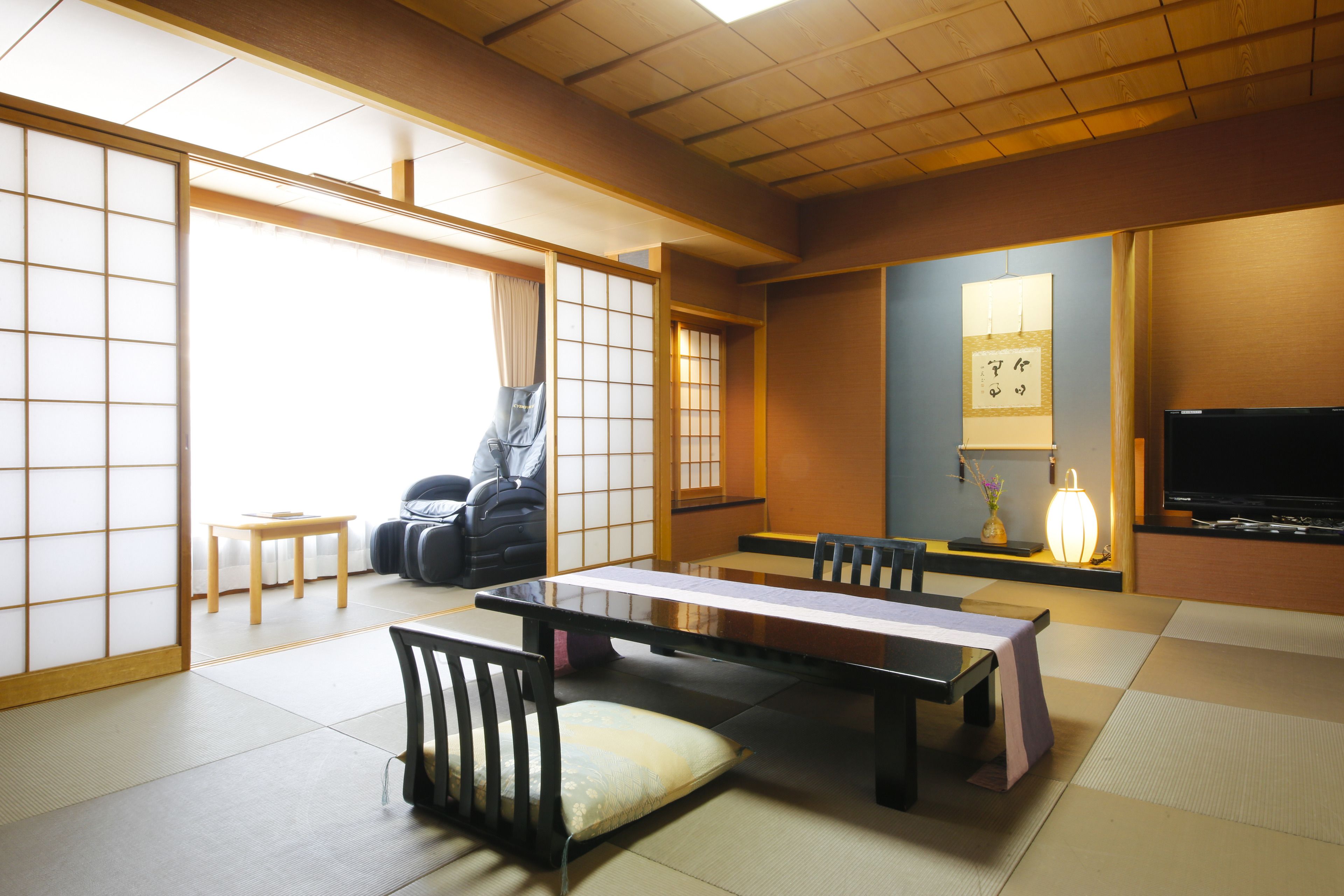 A traditional Japanese room with tatami flooring, a low table with cushions, and a television.