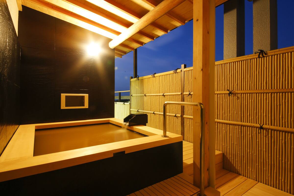 Un área de hidromasaje de madera con una valla de bambú y una terraza de madera.