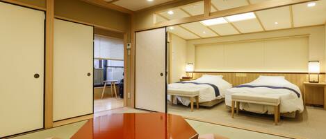 Une chambre d’hôtel de style japonais traditionnel, avec un sol recouvert de tatamis, une table en bois, deux lits et un grand miroir qui reflète la pièce.