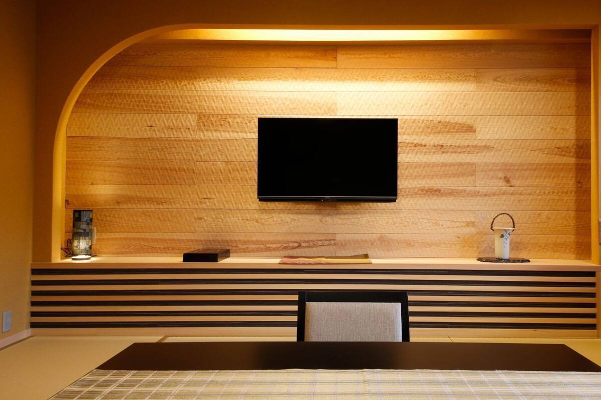Una sala de estar moderna con un televisor de pantalla plana montado en una pared de madera, un sofá y una mesa de comedor con un mantel individual.