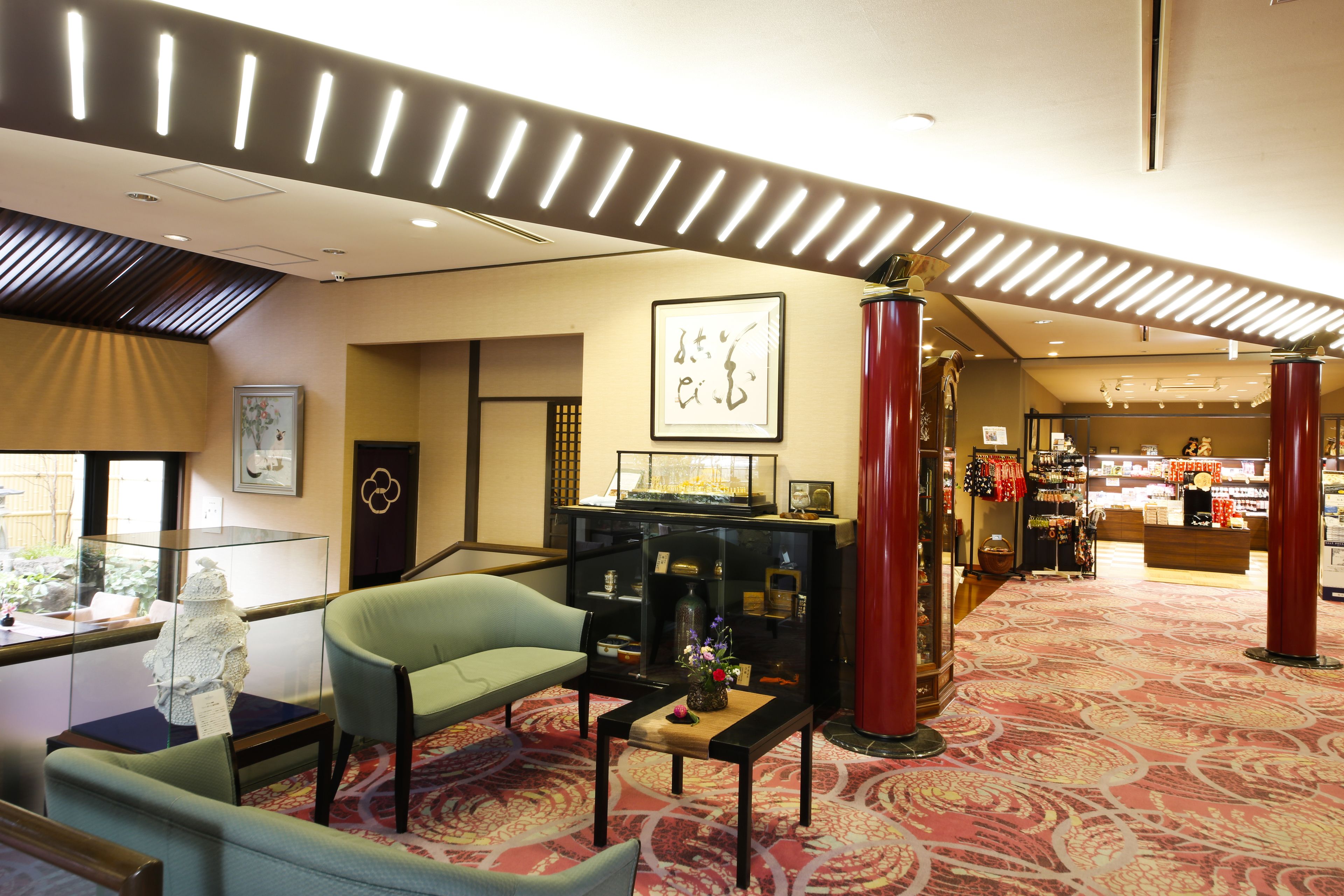 Eine Hotelhalle im traditionellen japanischen Stil mit einer Rezeption, einer Sitzecke und einer Ausstellung lokaler Handwerkskunst.
