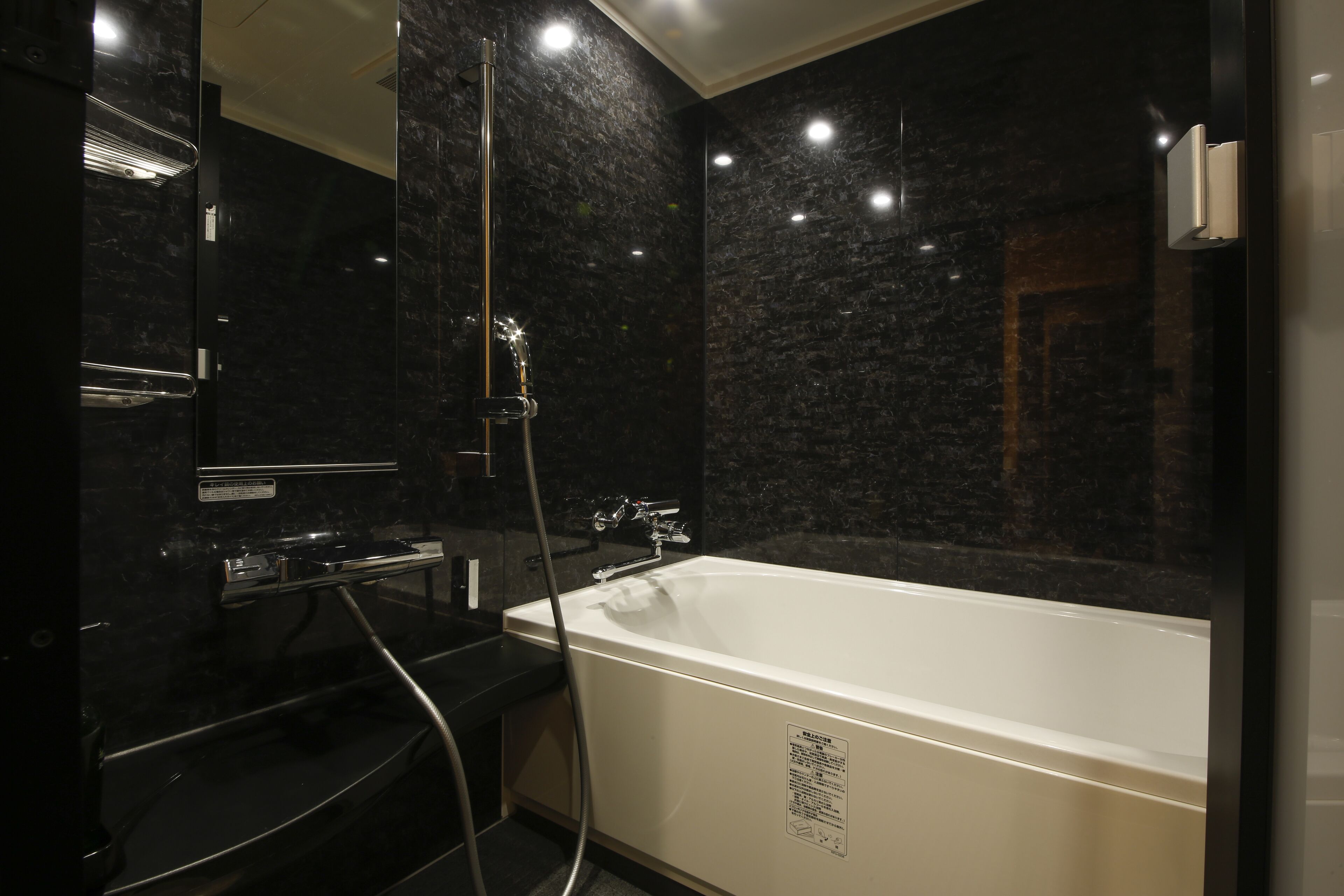 Un baño moderno con una bañera independiente, cabina de ducha con paredes de vidrio y pared de mármol oscuro.