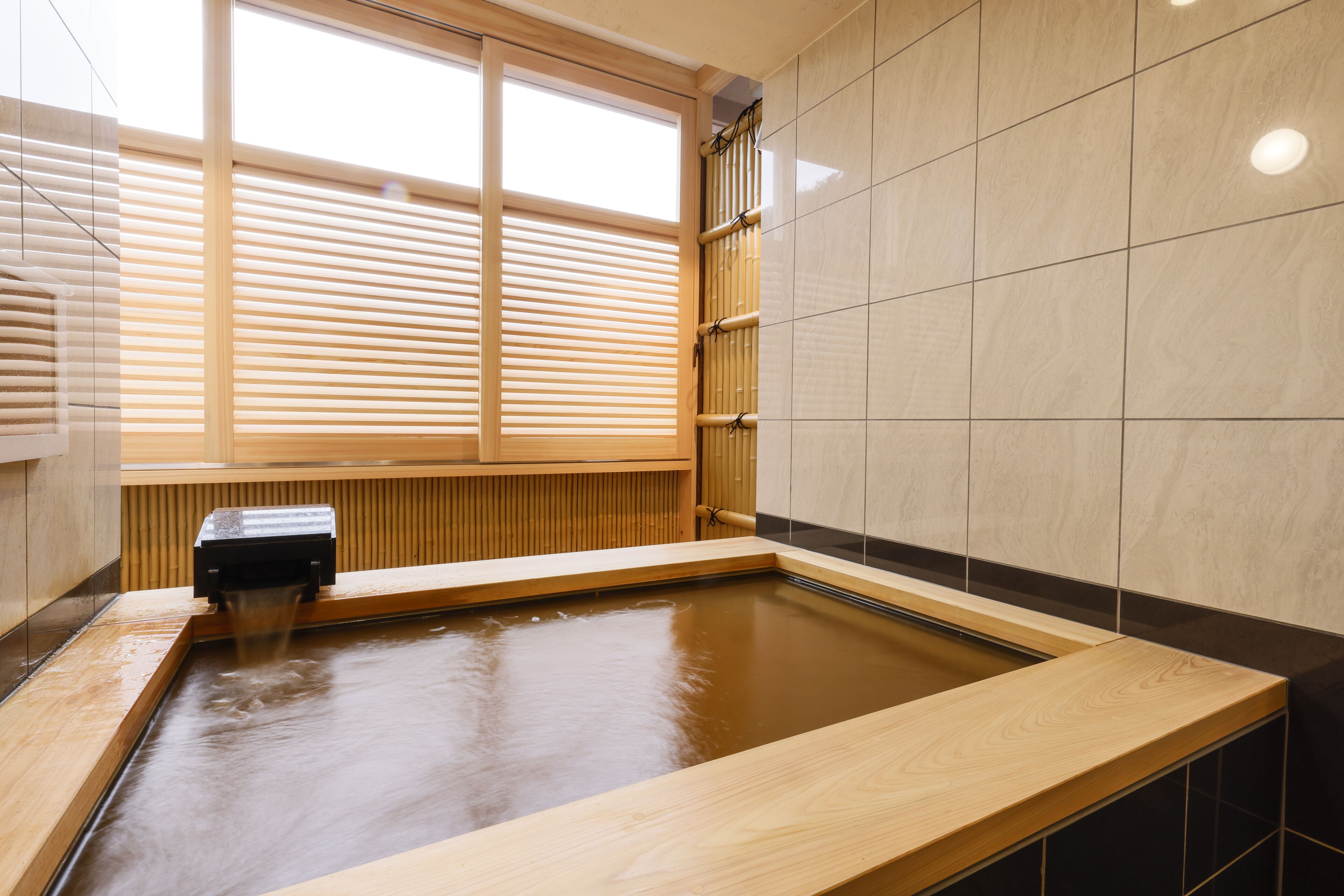 Ein modernes Spa mit einer Holzbadewanne, einem Fenster mit Jalousien und gefliesten Wänden.
