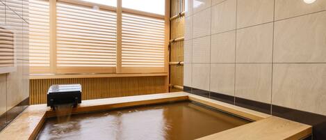 Un spa moderno con una bañera de madera, una ventana con persianas y paredes de azulejos.
