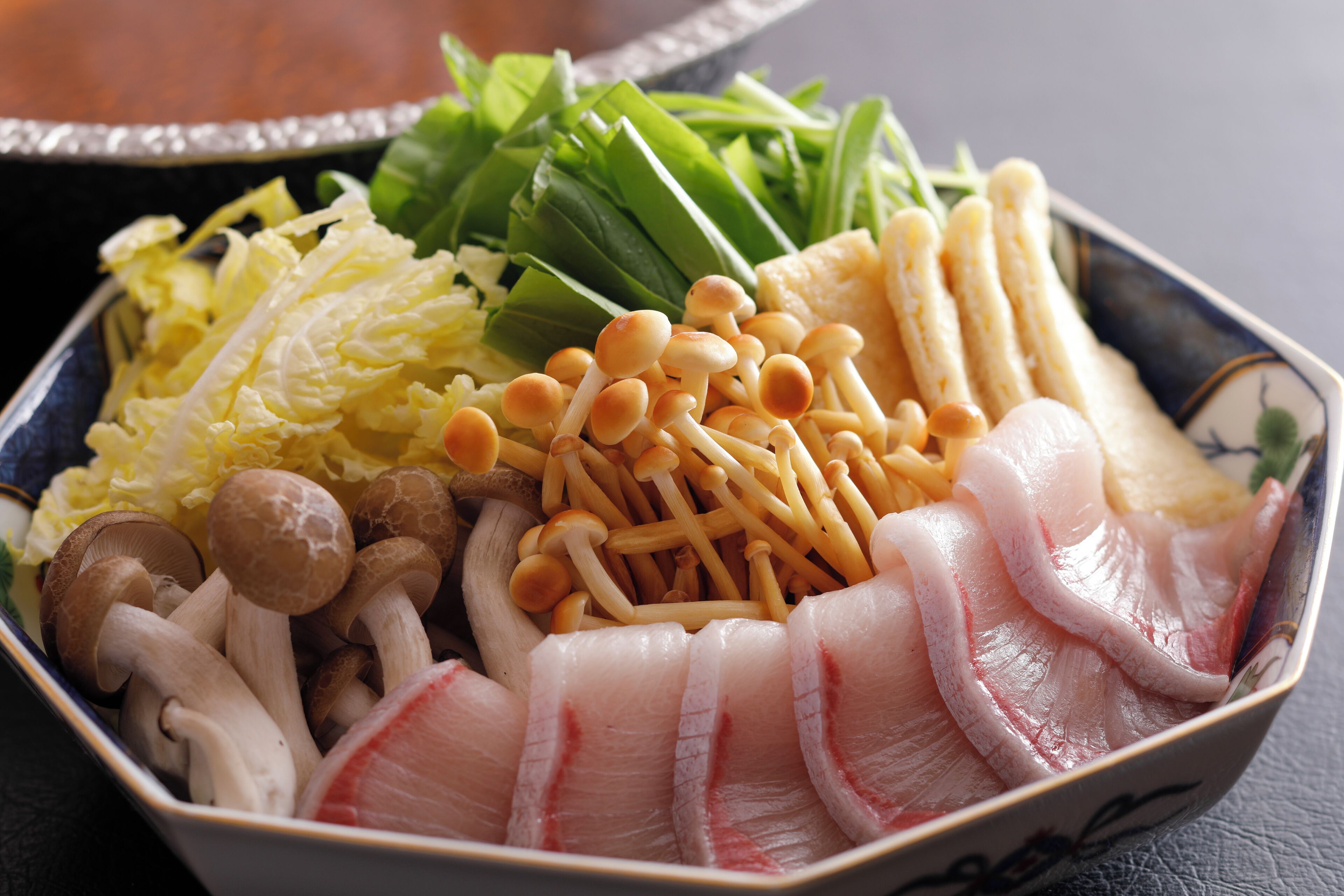 A bowl of assorted raw ingredients including mushrooms, green vegetables, and fish slices.