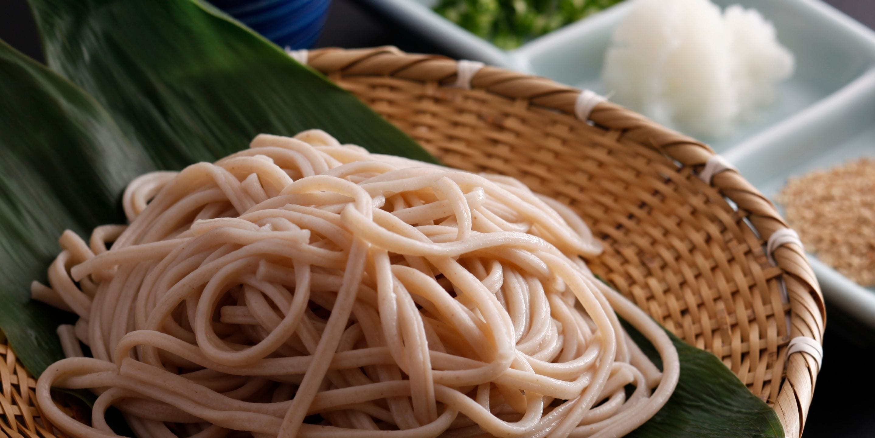 A woven basket filled with noodles placed on a green leaf.