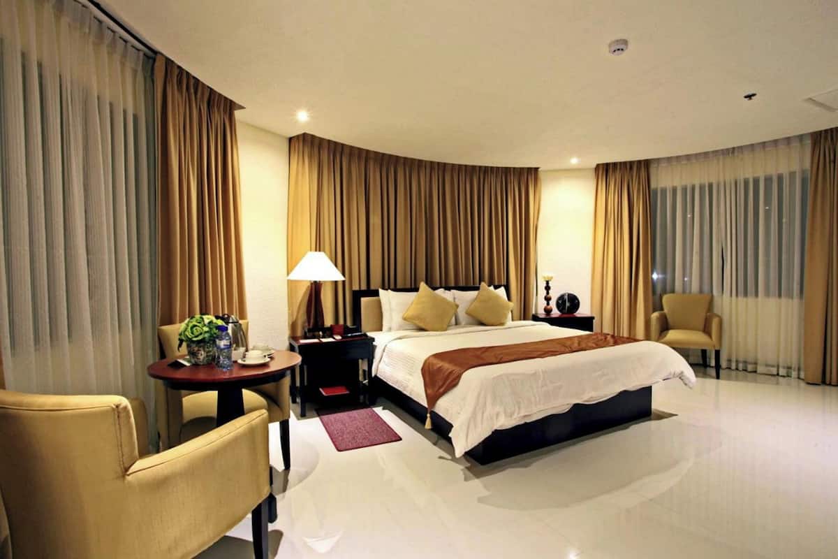 A hotel room with a large bed, a desk with a lamp, a chair, and a nightstand.