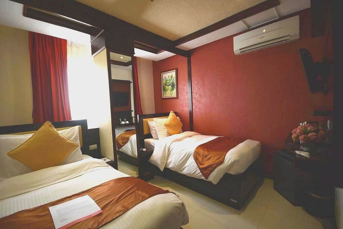 A hotel room with two beds, a red wall, an air conditioning unit, and a small table with flowers.