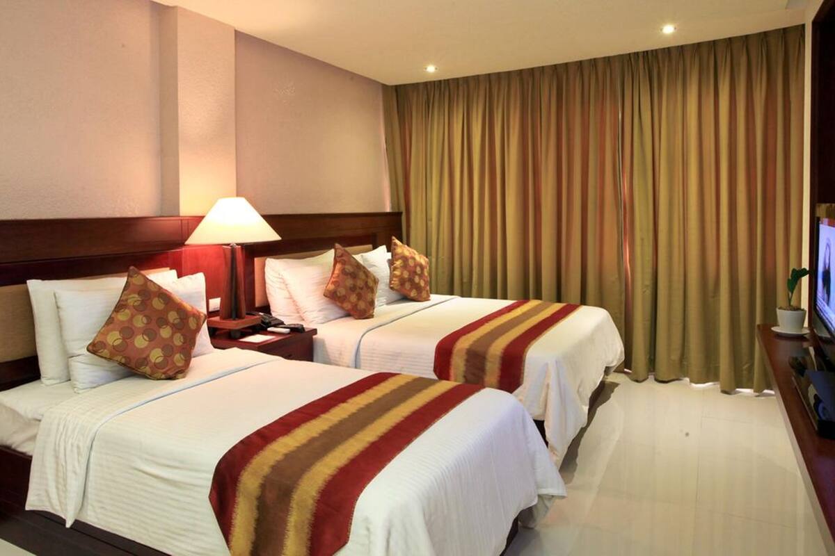 A hotel room with two beds, a TV, and a desk with a lamp.