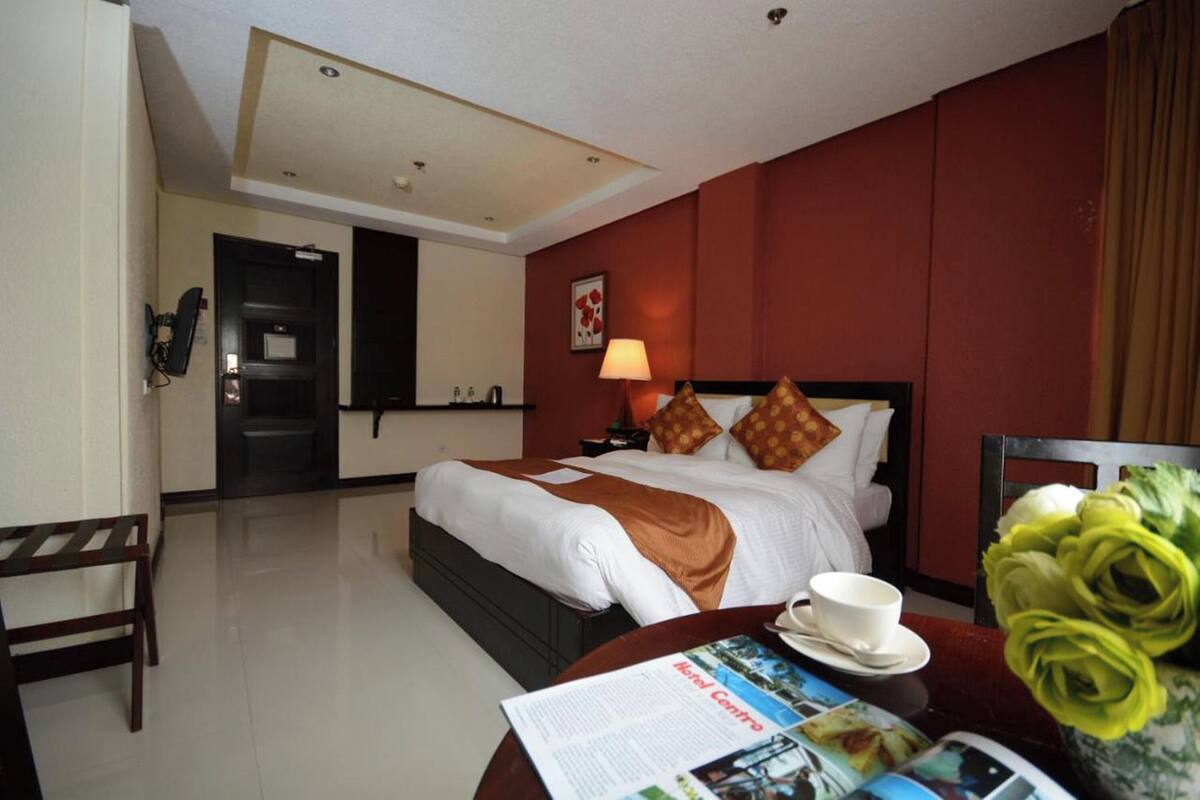A hotel room with a bed, bedside table, lamp, and a table with a cup and a menu.