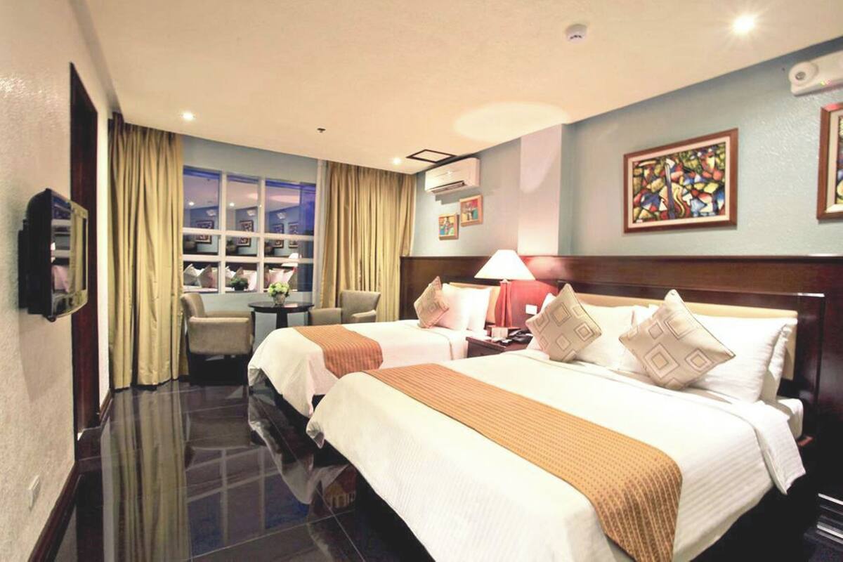 A hotel room with two beds, a desk, a chair, and a window with curtains.