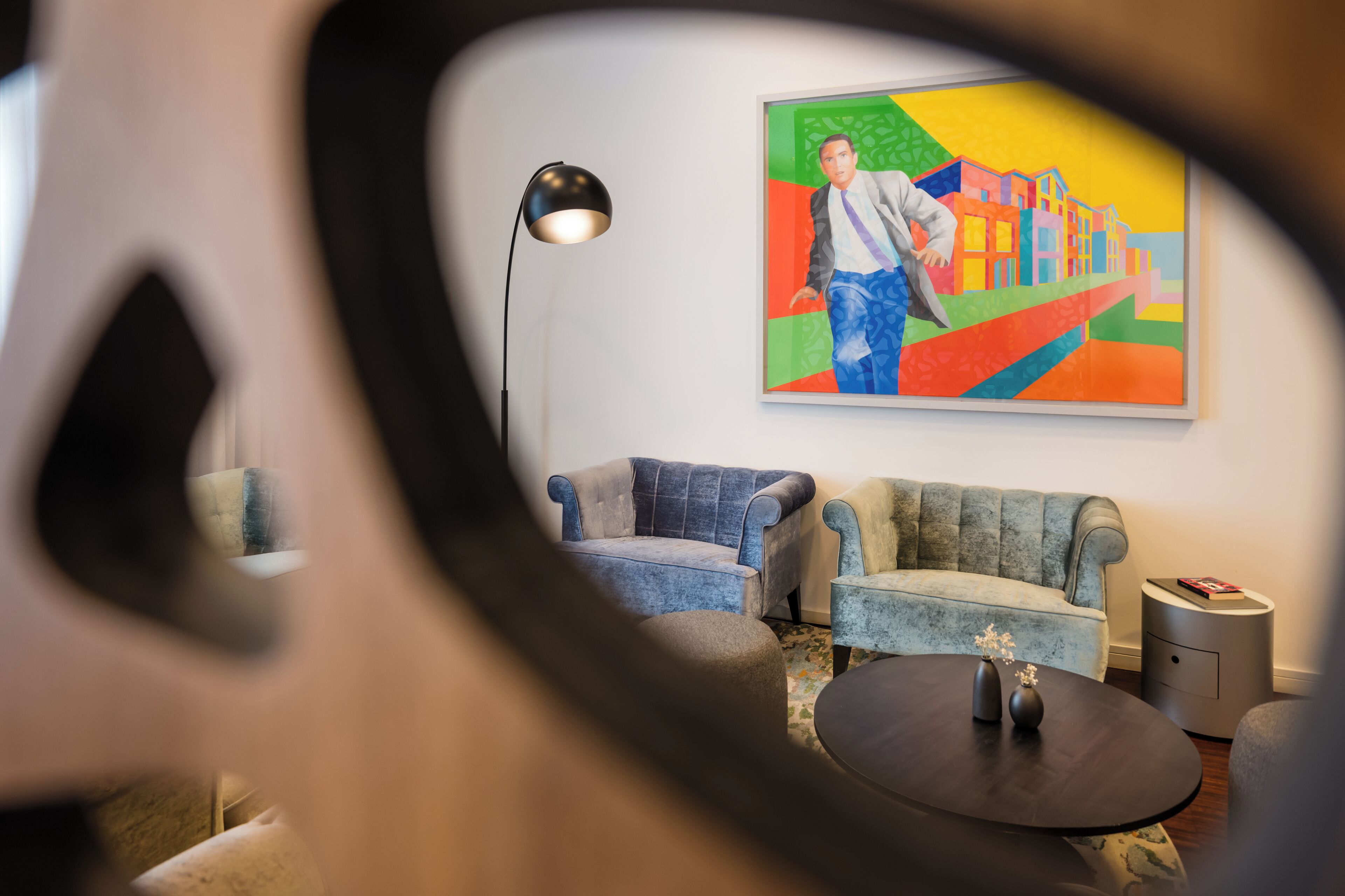 Ein modernes Wohnzimmer mit Sofa, Sessel und Couchtisch. Ein Bild hängt an der Wand, und eine Lampe steht auf einem Beistelltisch.