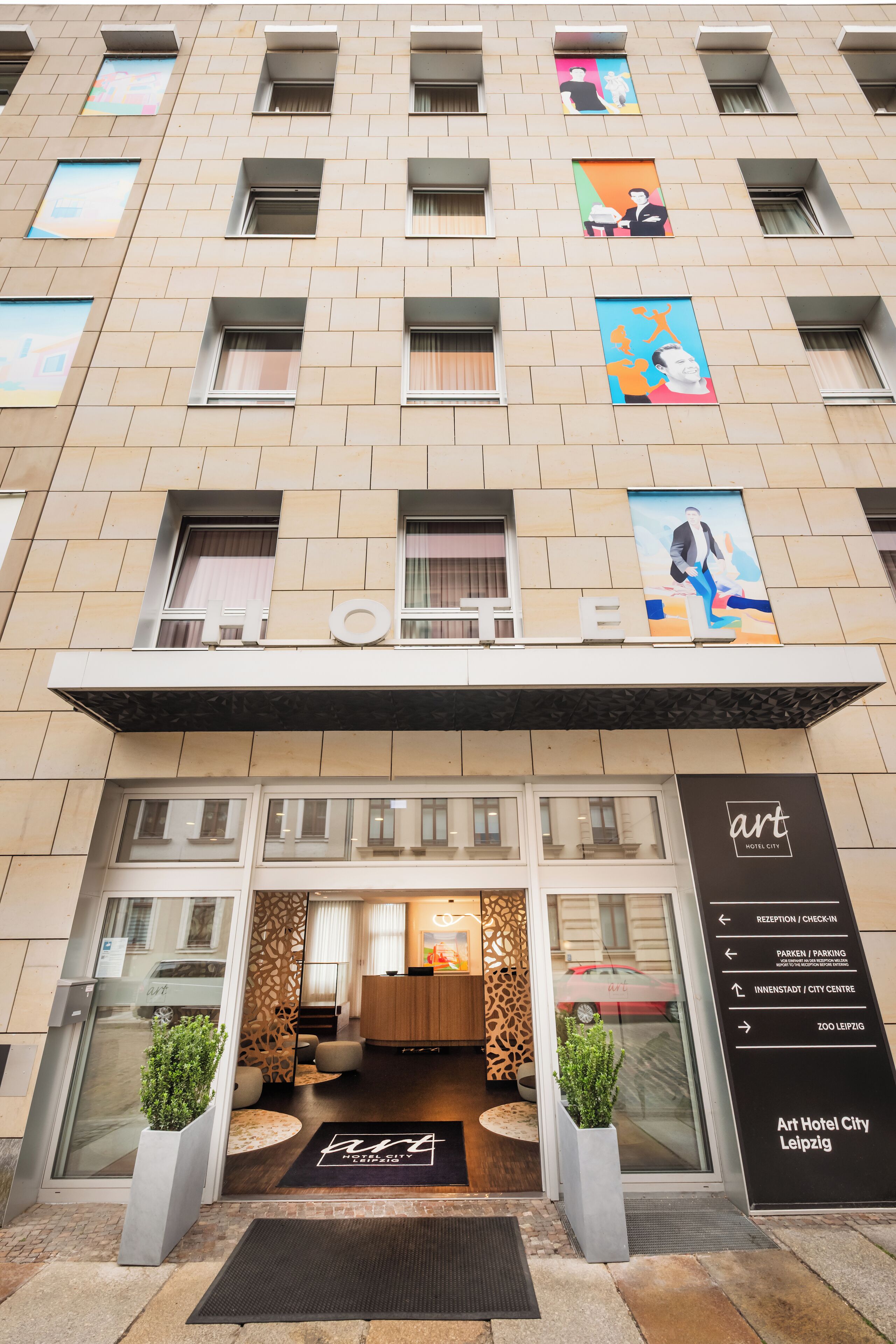 A hotel entrance with a modern facade, glass doors, and a reception area with a wooden counter.