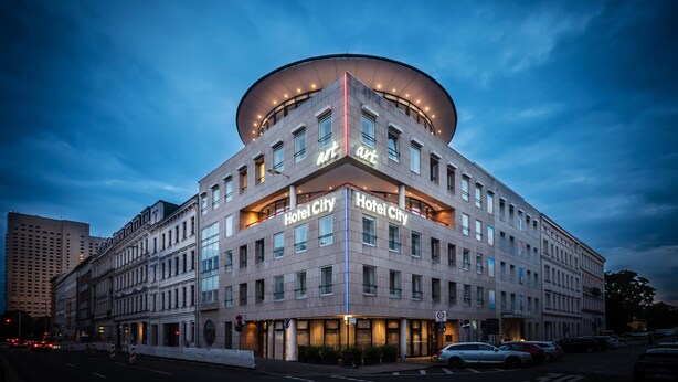 A hotel with a modern design, featuring a prominent circular rooftop structure and illuminated signage. - Art Hotel City Leipzig (Leipzig)