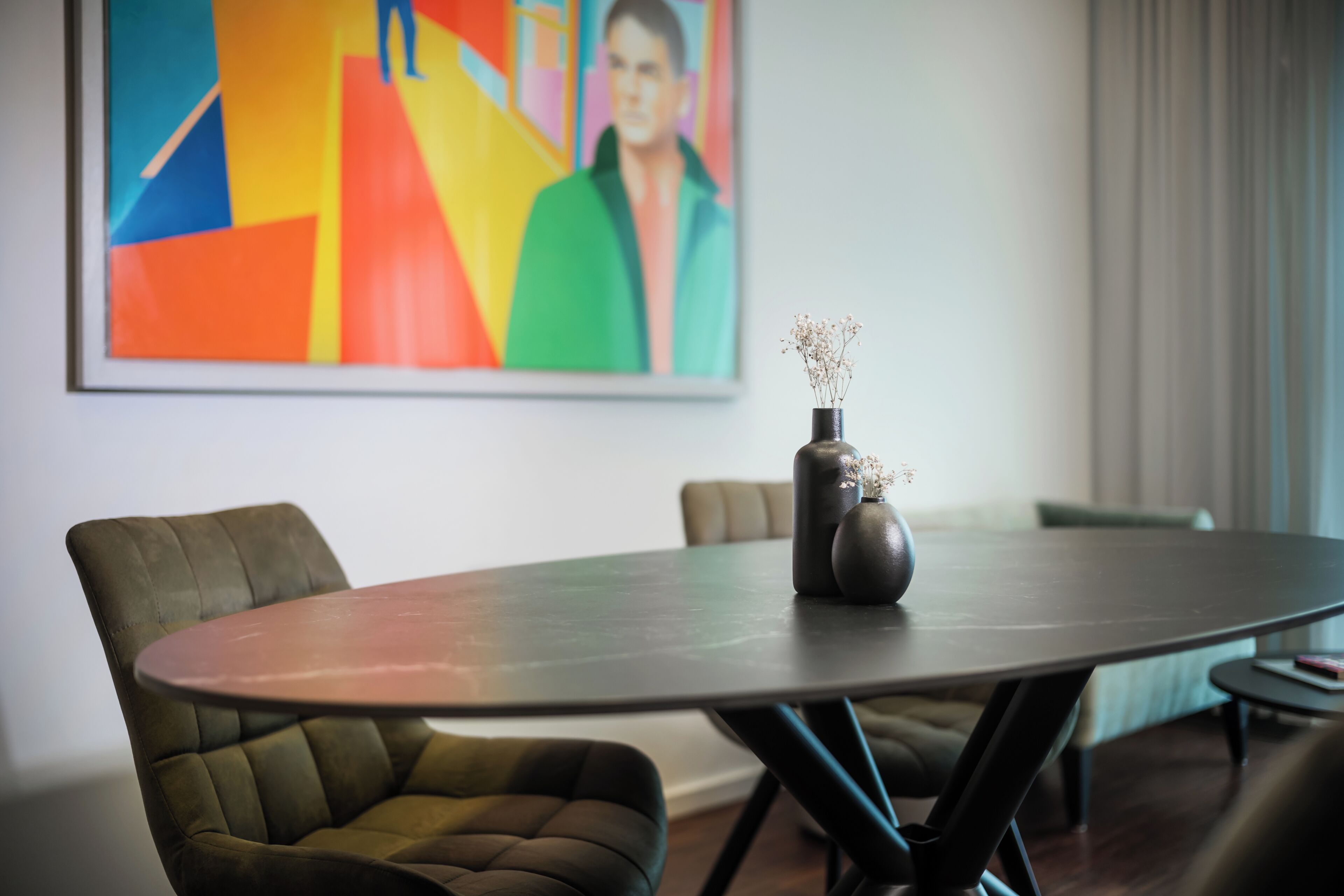 A conference room with a round table, two upholstered chairs, a vase with flowers, and a colorful abstract painting on the wall.