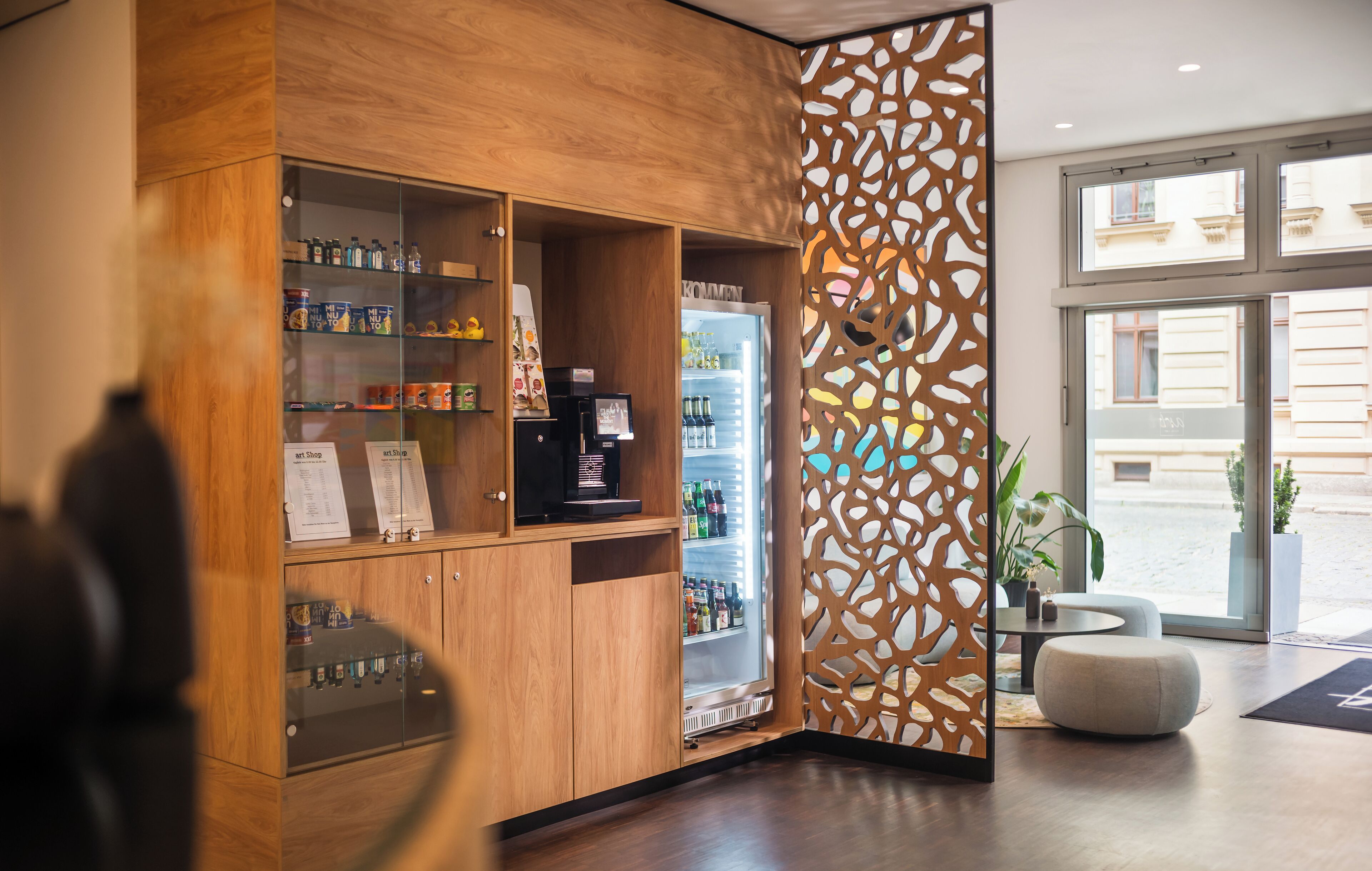 Un espace d’accueil moderne avec des meubles en bois, un réfrigérateur pour boissons et un élément de séparation décoratif.