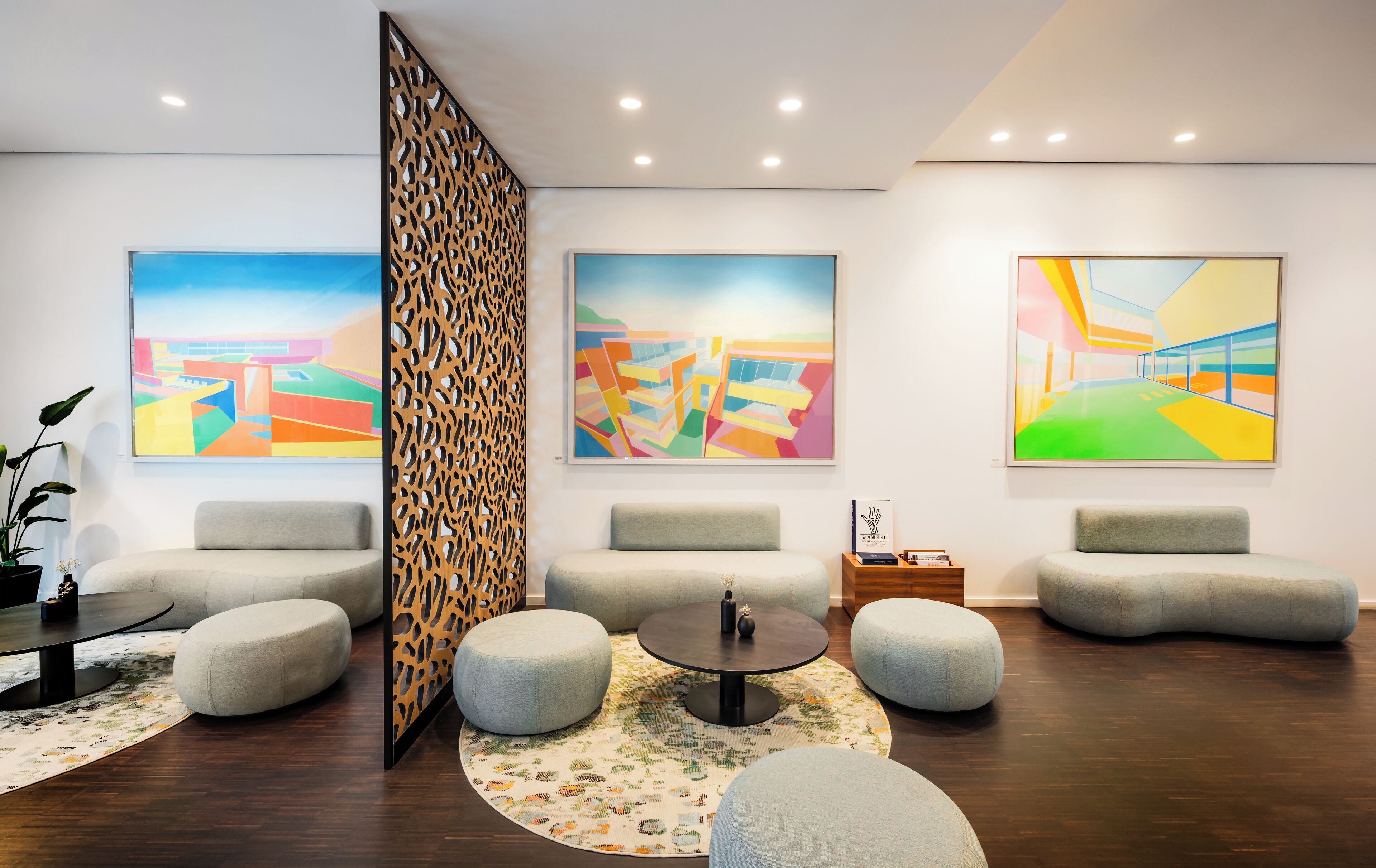 Un hall d’entrée moderne agrémenté de peintures abstraites, de canapés gris, d’une table ronde et d’un élément de séparation décoratif.