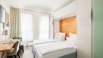 A hotel room with a bed, a desk, a chair, a lamp, and a window with curtains.