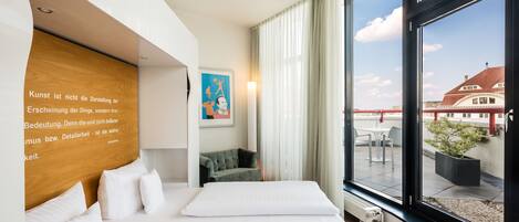 Habitación de hotel moderna con una cama grande, un cabecero de madera, vistas a la ciudad y un sofá verde.