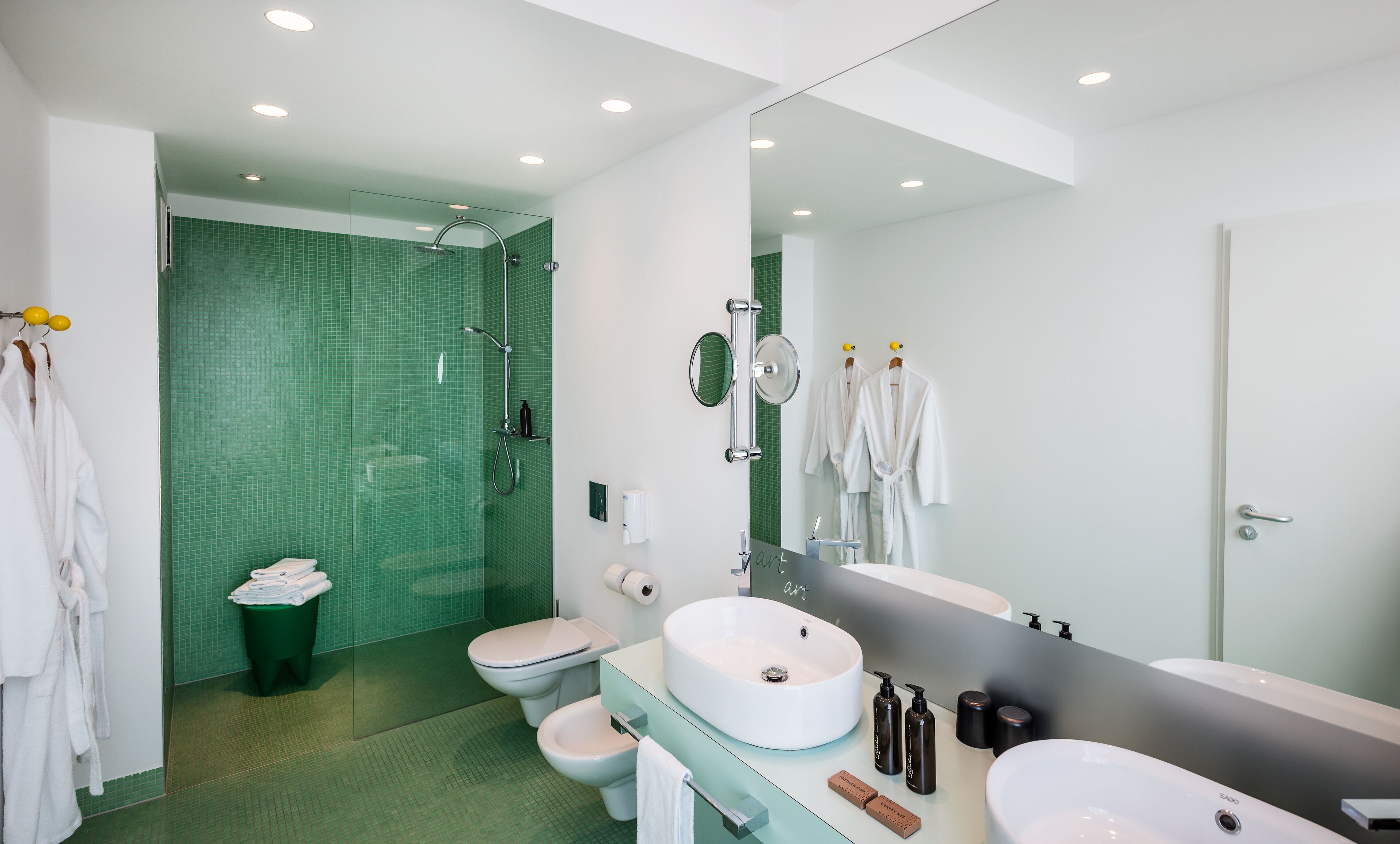 A modern bathroom with a large mirror, two sinks, a shower, and a toilet.