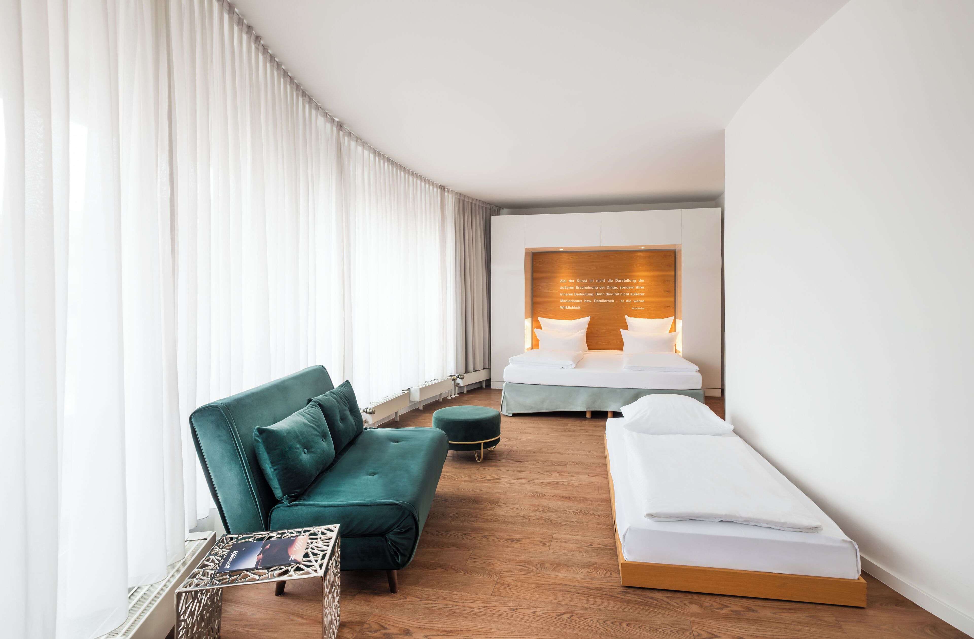 A modern hotel room with a green sofa, a single bed, and a small table.