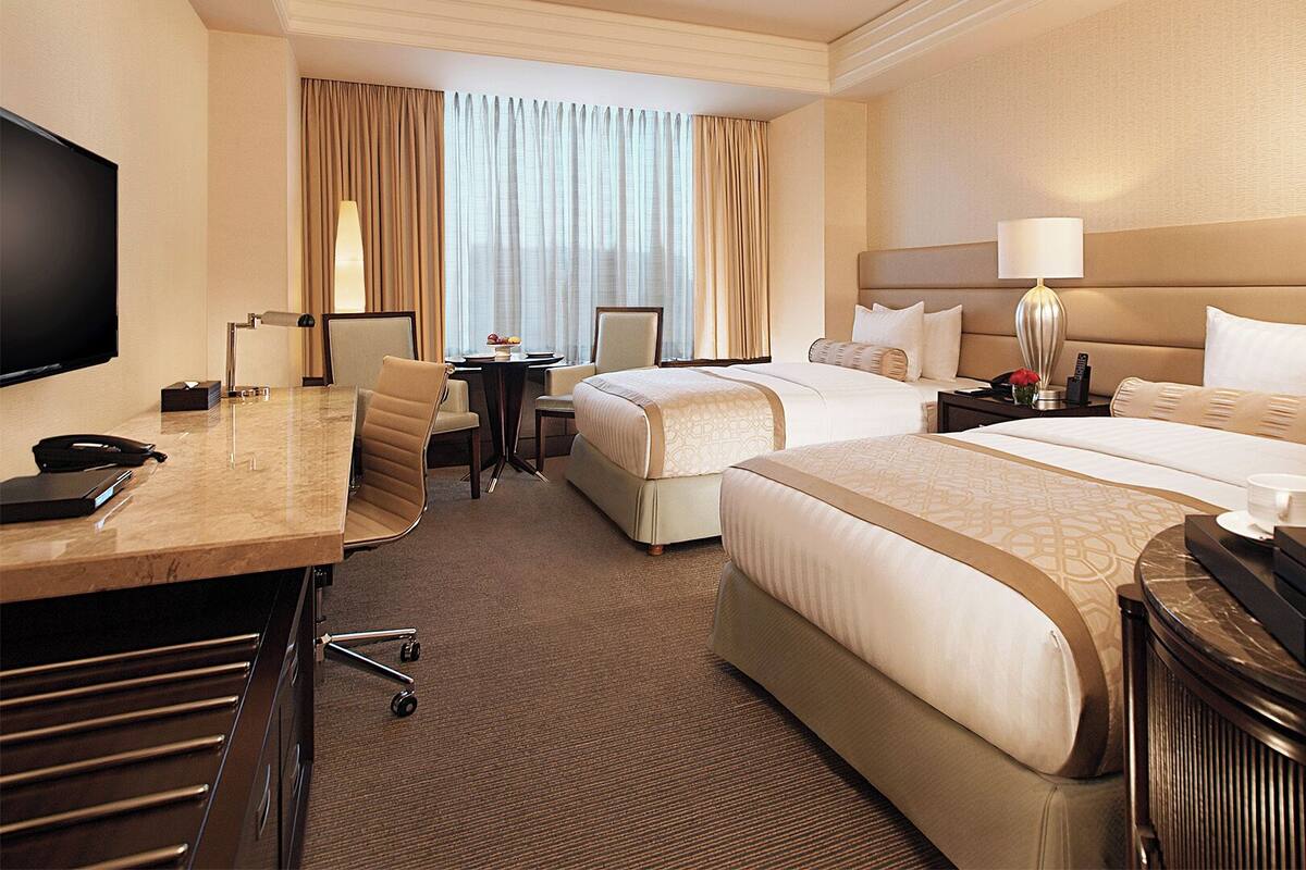 A hotel room with two beds, a desk with a telephone, a TV, and a small table with a lamp.