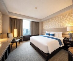 Una habitación de hotel con una cama grande, un escritorio, una silla y un ventanal con cortinas.