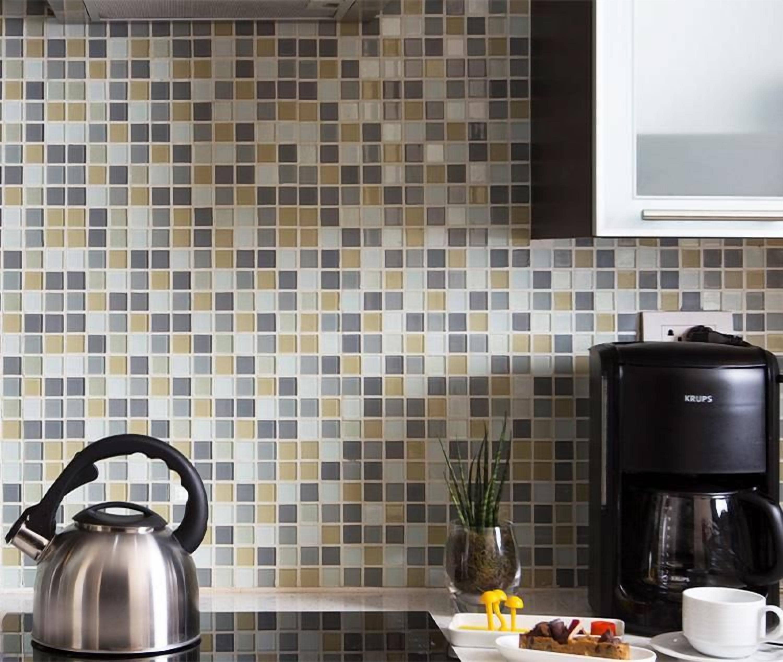 A kitchen with a tiled backsplash, a kettle, a coffee maker, and a small potted plant.
