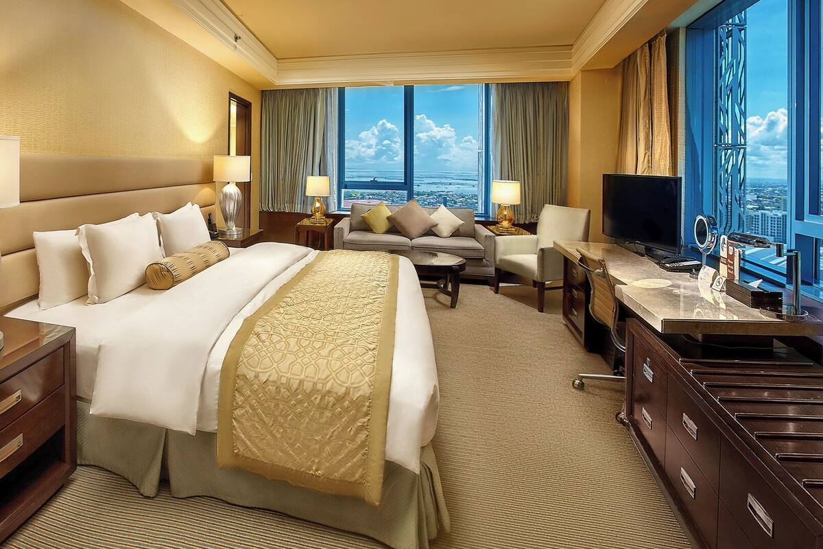 A hotel room with a large bed, a desk, a TV, and a view of the ocean.