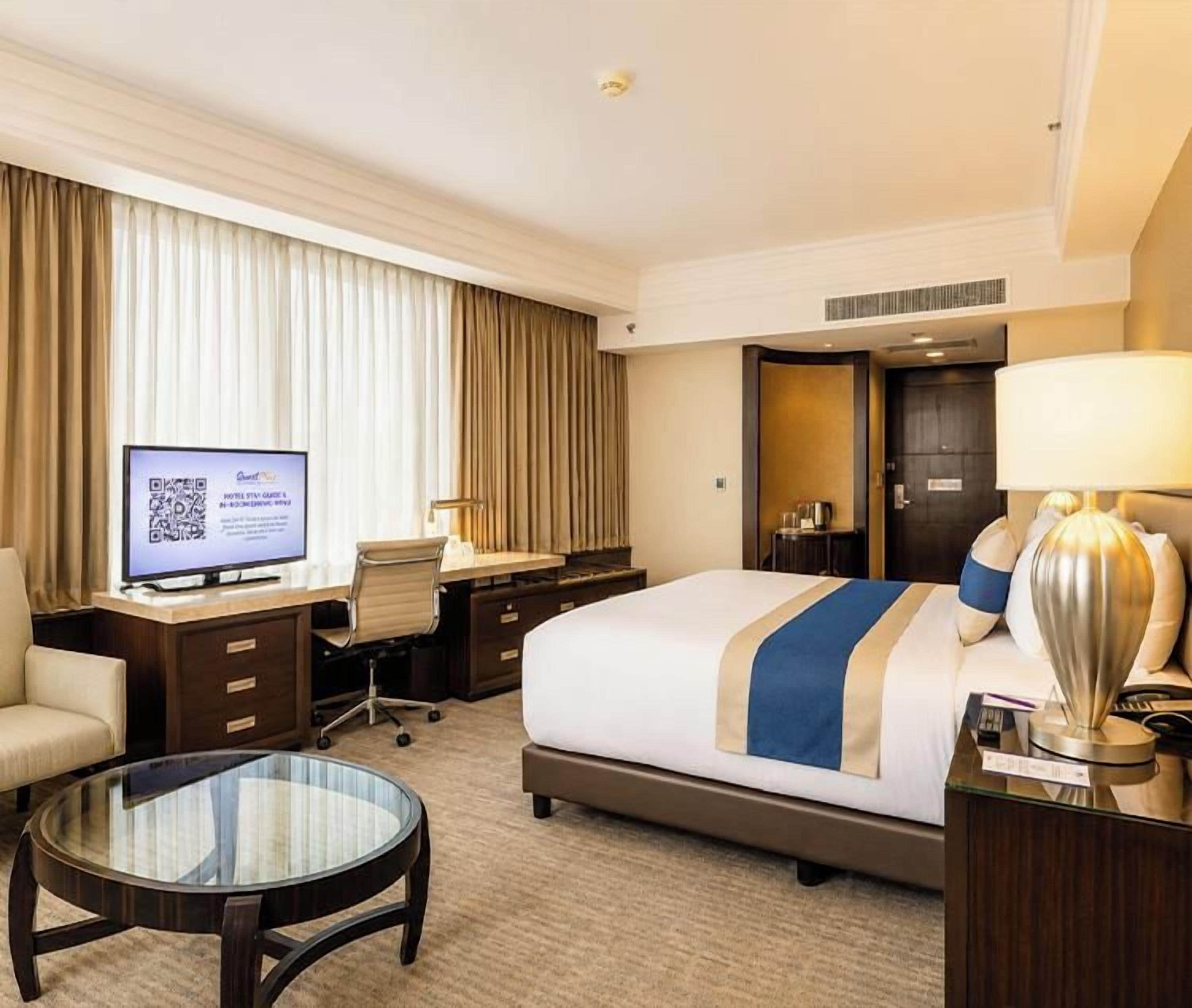 Habitación de hotel con una cama, un escritorio, una silla, un televisor y una lámpara.