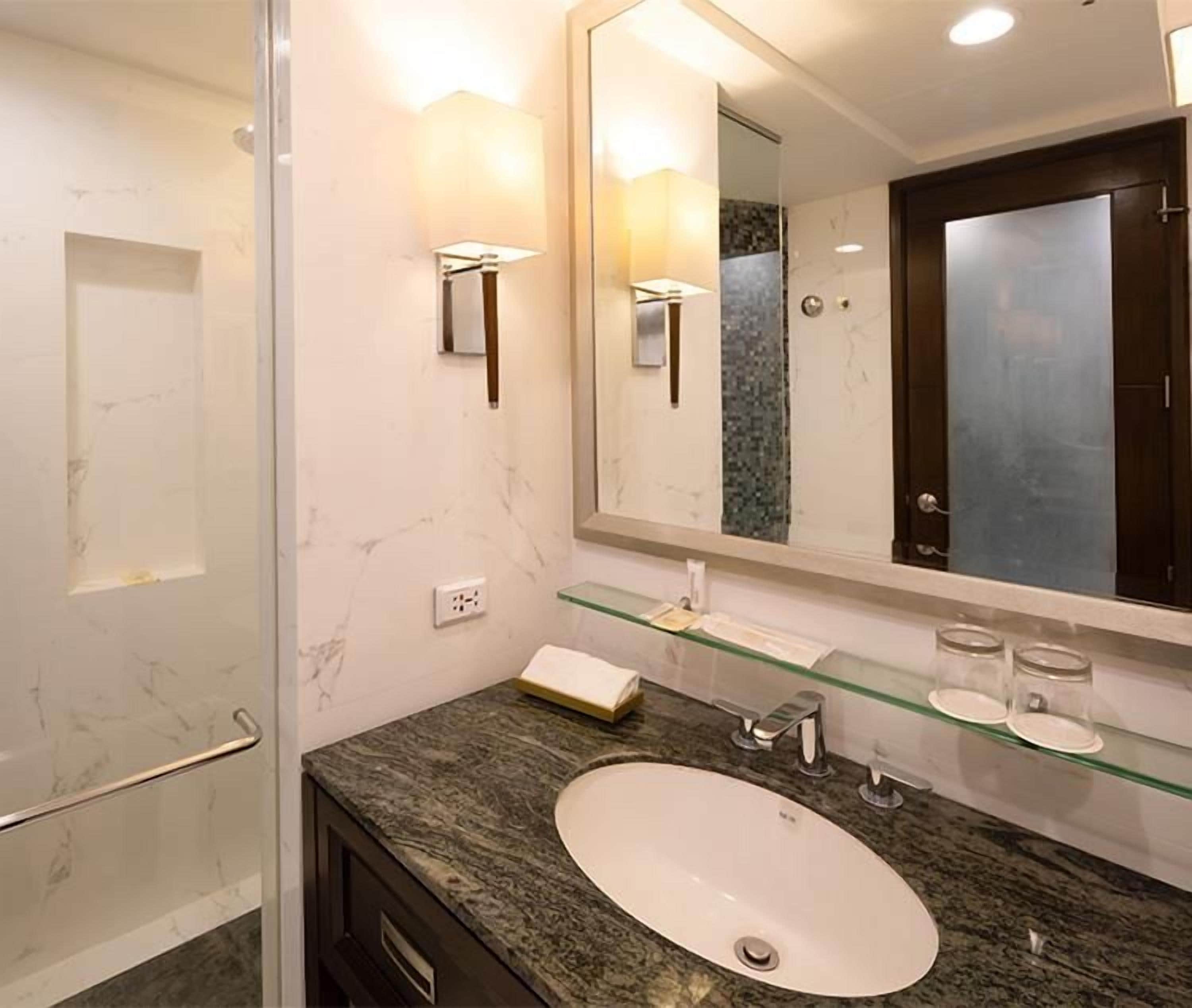 Un baño con cabina de ducha de vidrio, pared revestida de mármol, lavamanos blanco y un espejo grande.