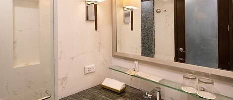 A bathroom with a glass shower enclosure, a marble-tiled wall, a white sink, and a large mirror.