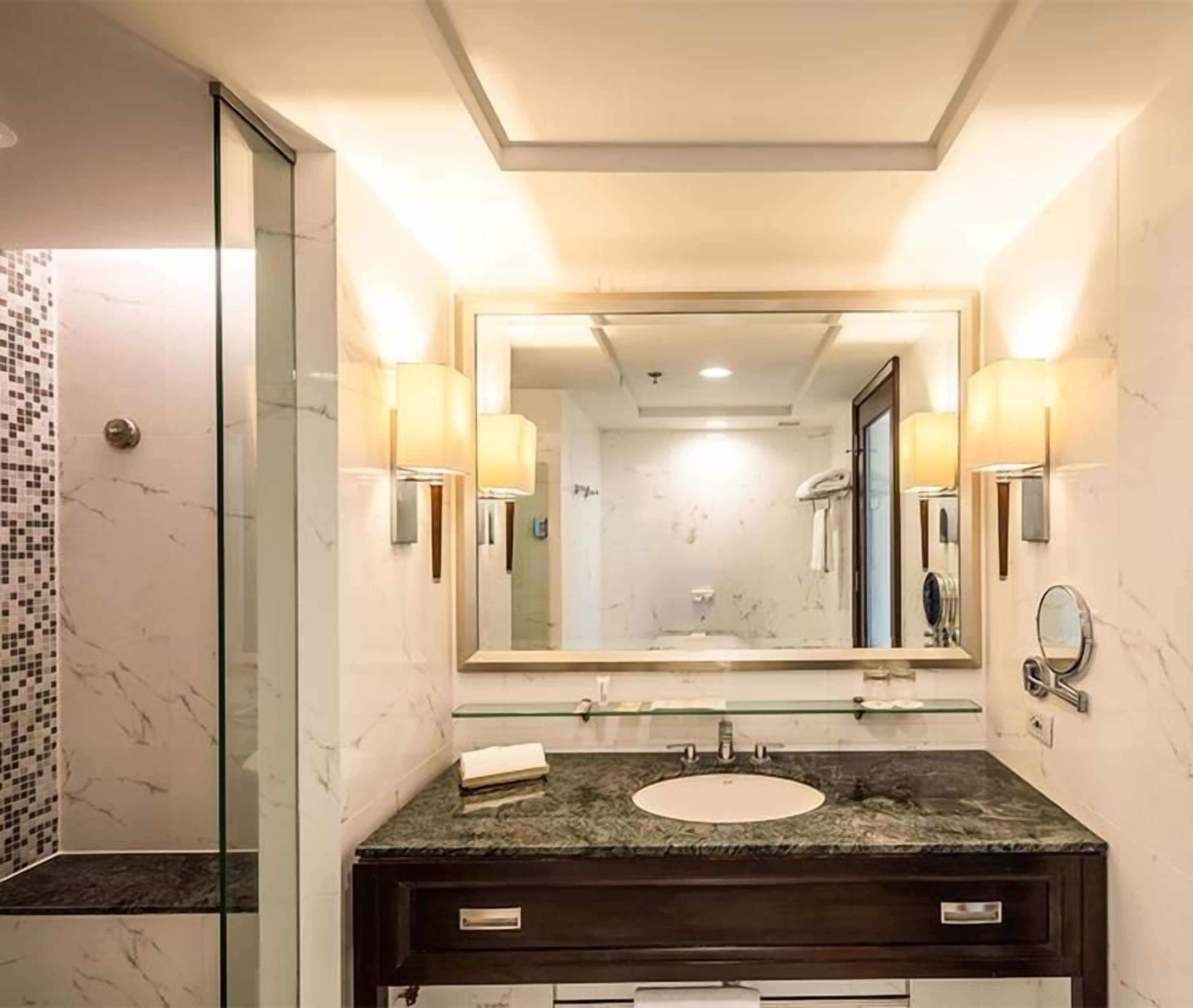 A modern bathroom with a glass shower enclosure, a marble-tiled shower area, a dark wooden vanity with a sink, and wall-mounted lighting.
