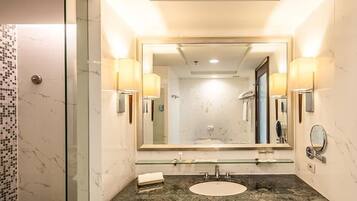 A modern bathroom with a glass shower enclosure, a marble-tiled shower area, a dark wooden vanity with a sink, and wall-mounted lighting.